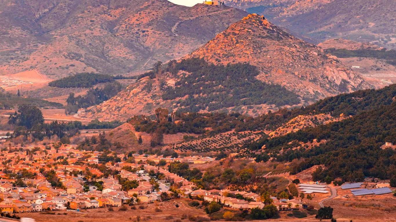 Valley town with houses California real estate, green trees, and mountains in the background.