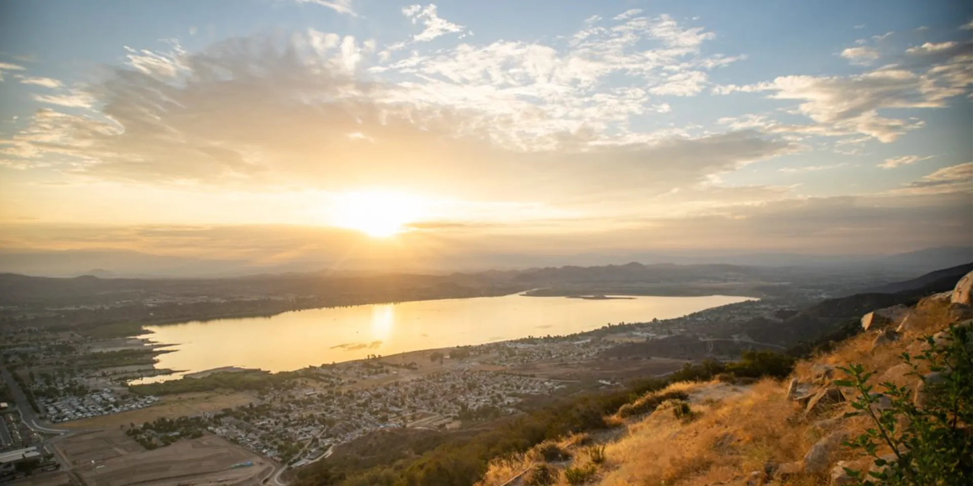 Lake at sunset with town, houses California real estate, and hills.