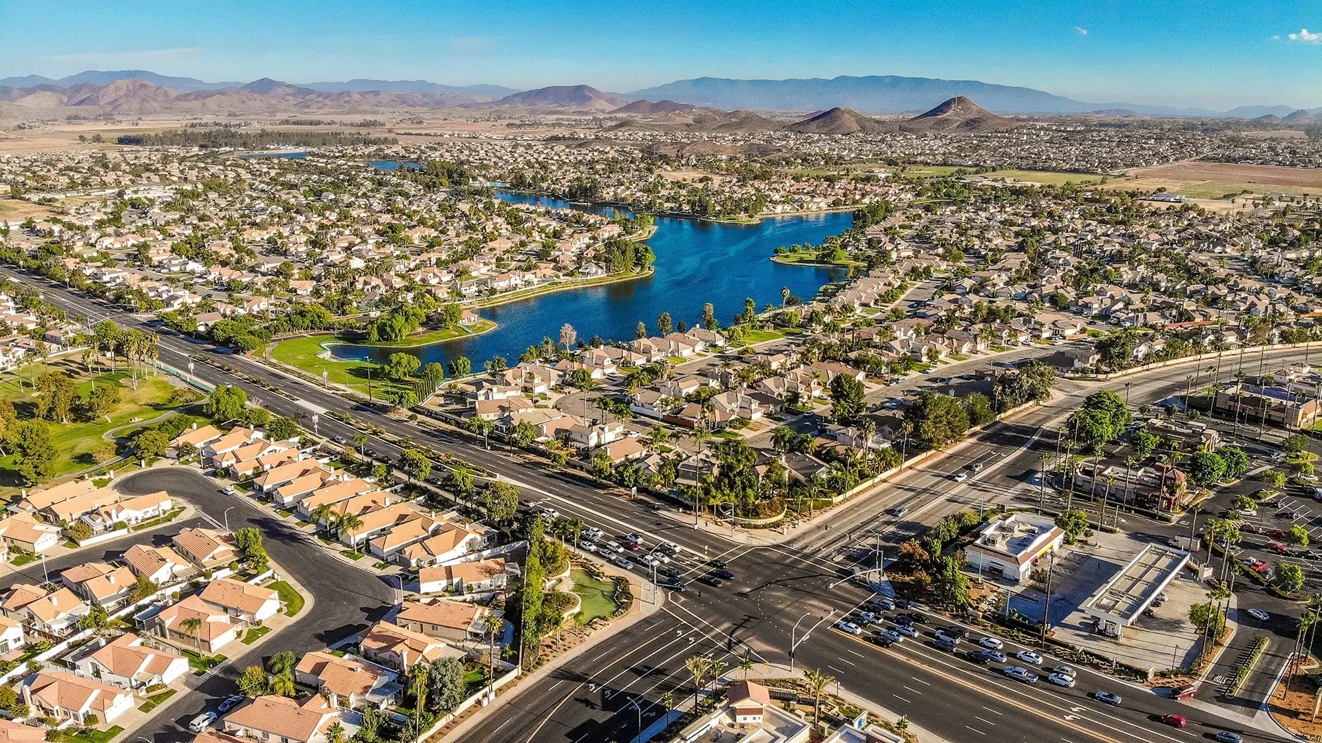 Aerial view of houses California real estate near water, roads, green spaces, and mountains.