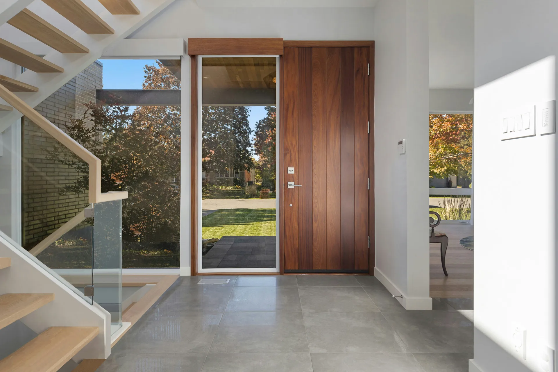 Entryway with wooden door, glass panel, and stairs with glass railing.