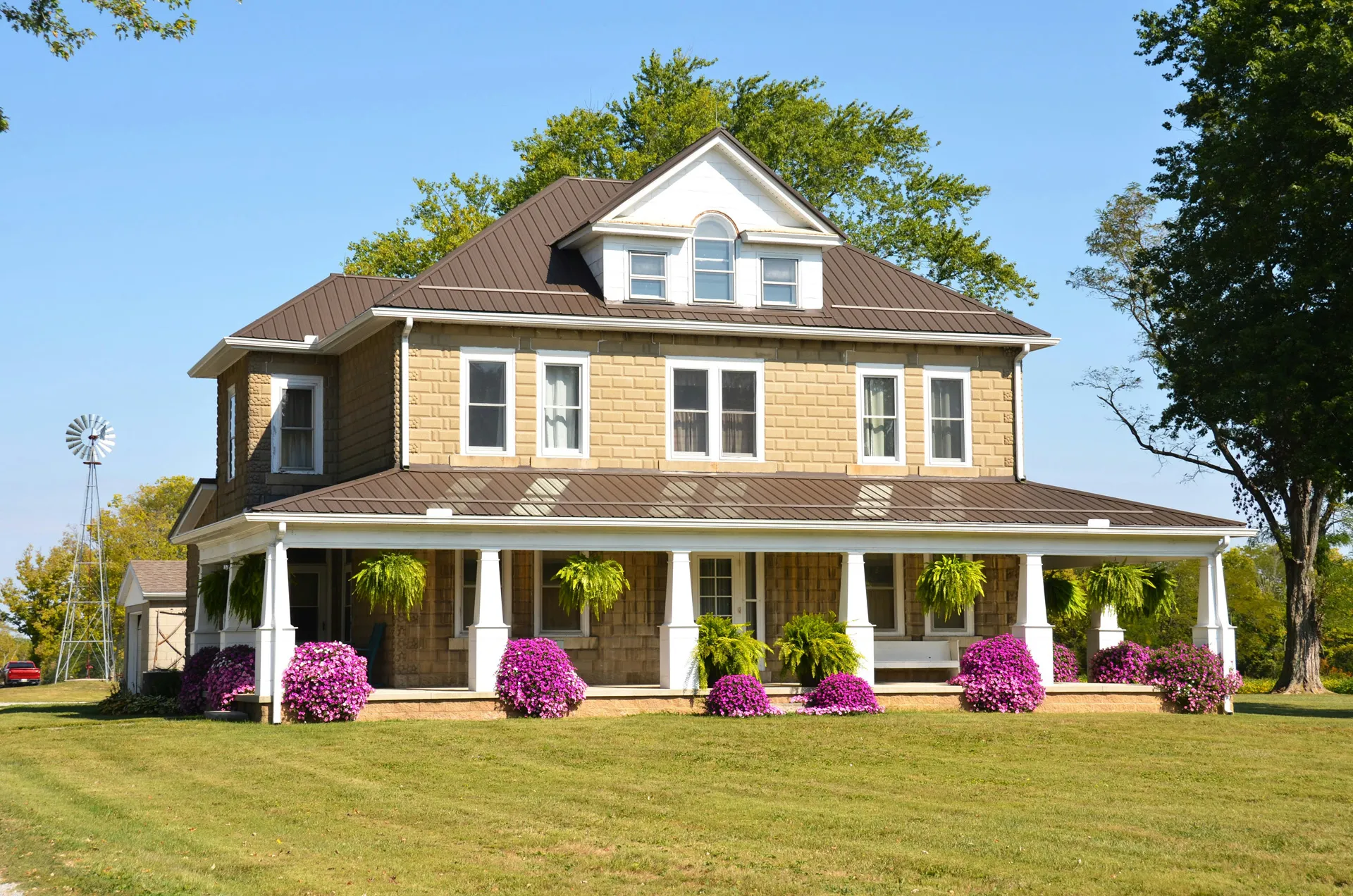 Two story house California real estate with porch, hanging plants, green lawn, and purple flowers.