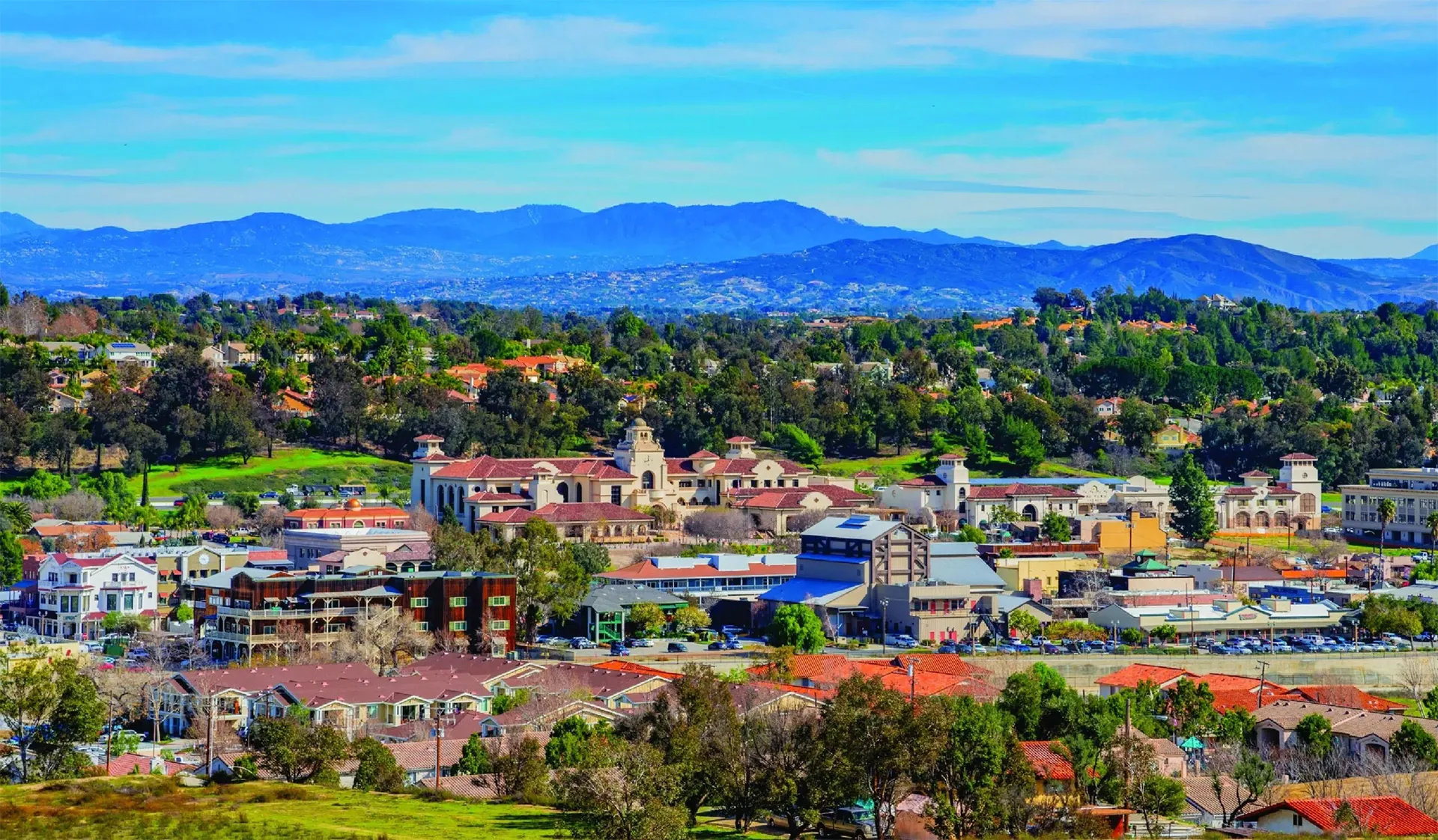Town in valley with houses California real estate, roads, hills, and green trees.