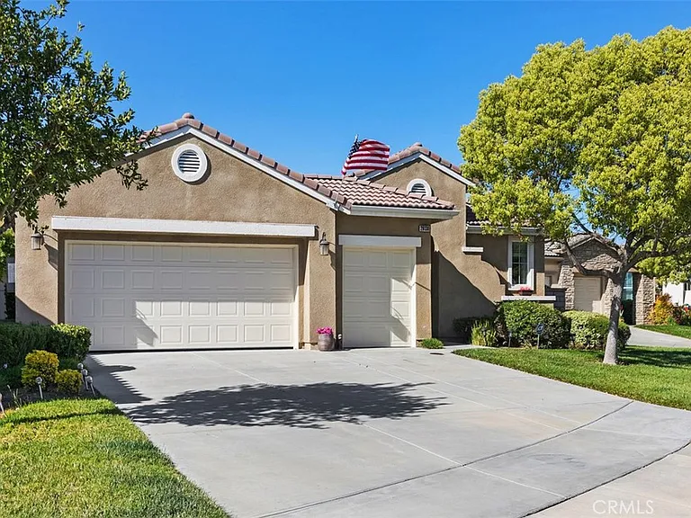 House California real estate with triple garage, American flag, large tree, and lawn.