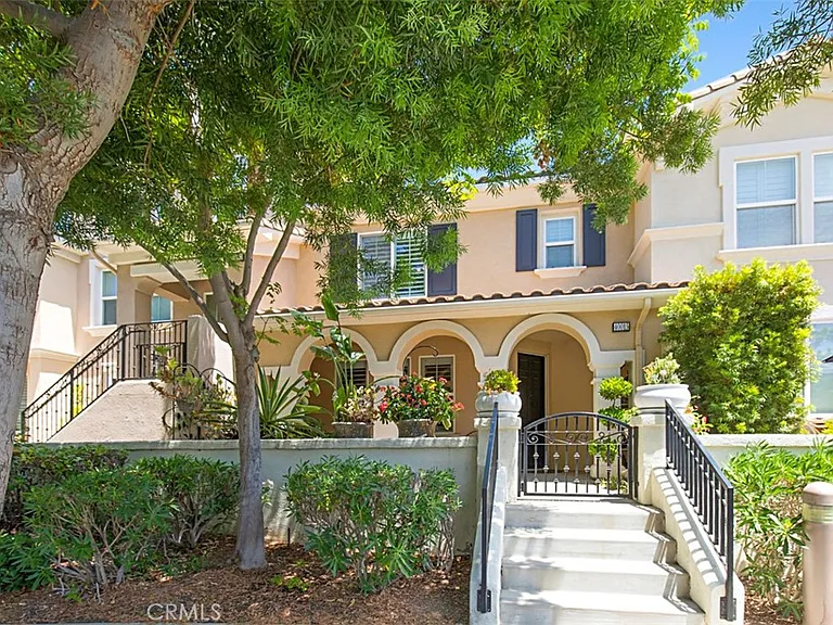 Two story Mediterranean house California real estate with arched porch, trees, bushes, and iron gate.