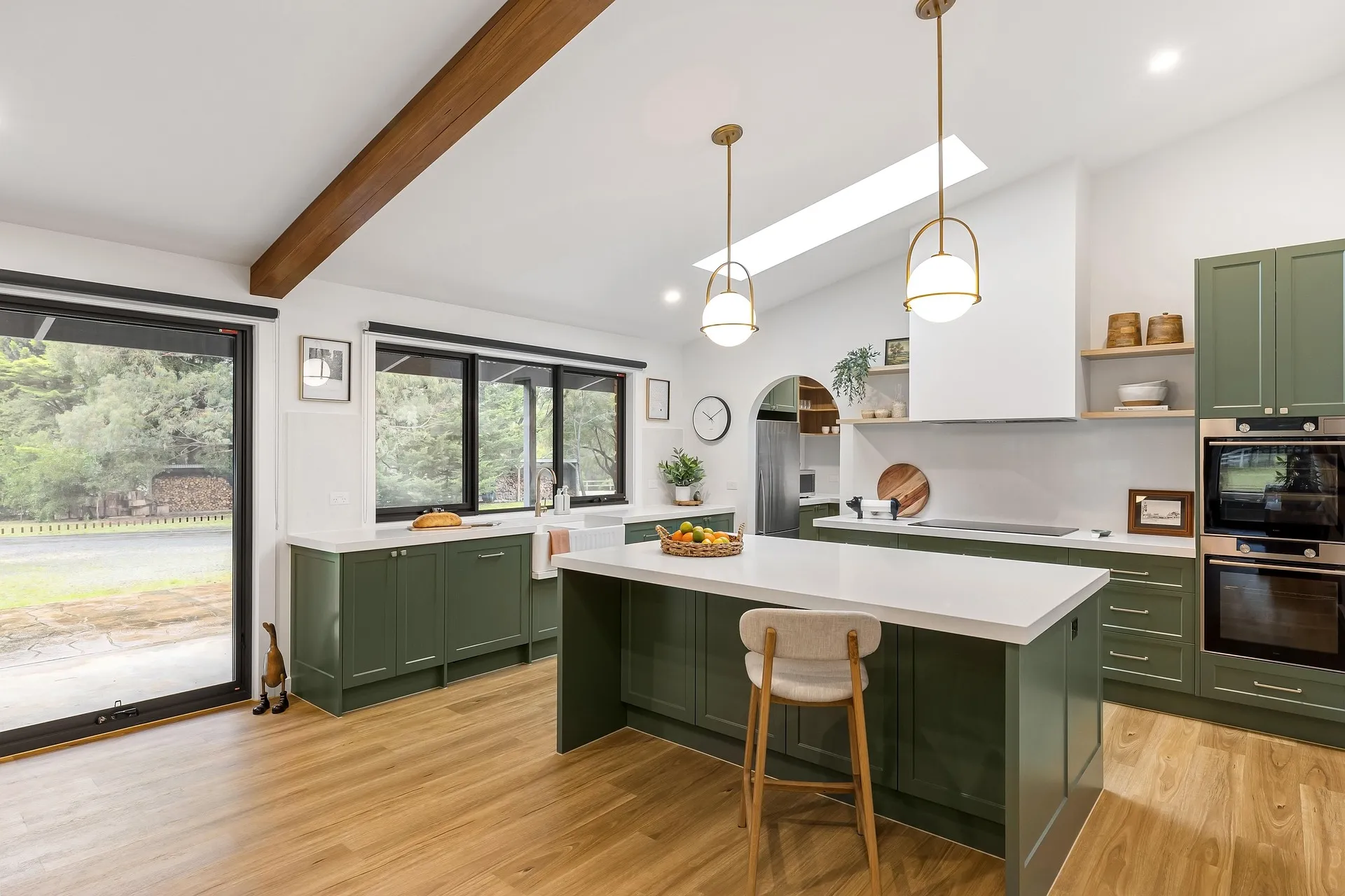 Kitchen with green cabinets, large island with seats, wooden floor, and big windows.